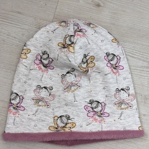 Puede incluir: Un gorro gris con forro de borreguito rosa. El gorro tiene un patr&oacute;n de hadas con alas y estrellas.