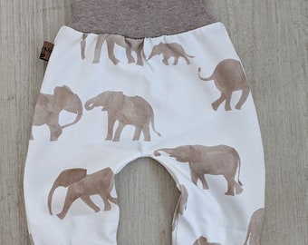 Könnte beinhalten: Weiße Babyhose mit braunem elastischem Bund und Bündchen. Die Hose hat ein Muster aus braunen Elefanten, die darauf gedruckt sind.