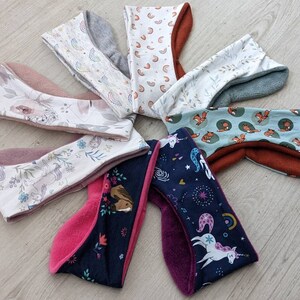 May include: A collection of colorful headbands with various patterns. Designs include floral, rainbows, foxes, and unicorns. The headbands have a soft, plush interior and are made of different fabrics, including fleece and patterned cotton.