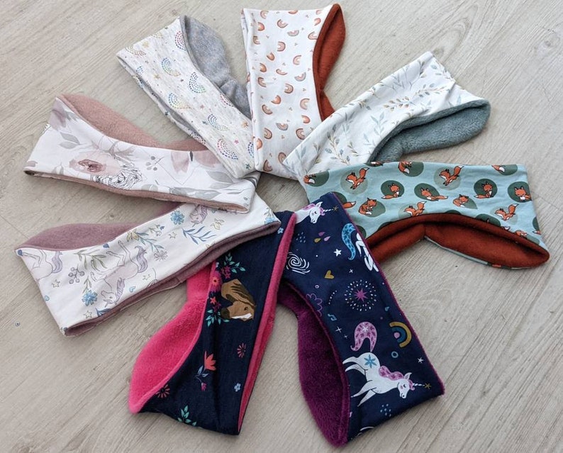 May include: A collection of colorful headbands with various patterns. Designs include floral, rainbows, foxes, and unicorns. The headbands have a soft, plush interior and are made of different fabrics, including fleece and patterned cotton.