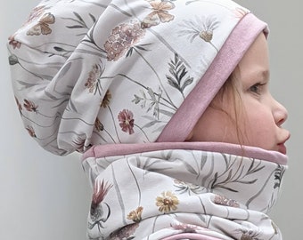 Puede incluir: Un conjunto de gorro y braga de cuello con estampado floral. El conjunto presenta un fondo blanco con un delicado estampado de flores y mariposas en tonos rosas, marrones y verdes. Los bordes están ribeteados con una tela rosa lisa.