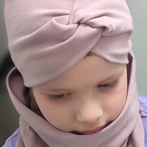 Peut inclure: Une jeune personne portant un bandeau turban rose clair et un cache-cou rose clair assorti.
