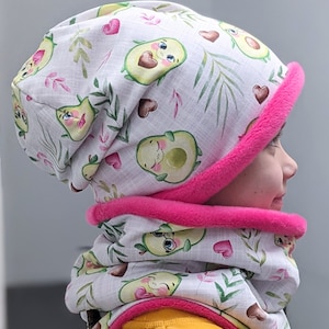 Może przedstawiać: Biały zestaw czapki i komina z różową lamówką. Tkanina ma powtarzający się wzór awokado z twarzami i sercami.