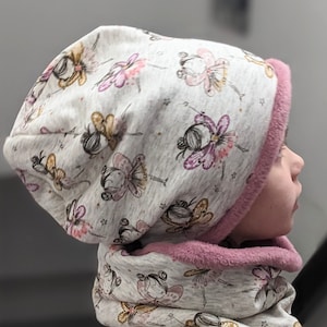 Puede incluir: Un gorro y una bufanda a juego de punto gris y rosa con un patr&oacute;n de hadas con alas y estrellas. El gorro tiene un forro de borreguito rosa.