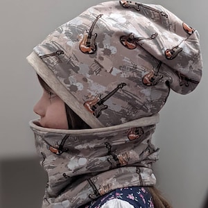 Op de afbeelding: Een beige muts en nekwarmer set met een gitaarprint. De muts is naar beneden gevouwen en de nekwarmer wordt om de nek gedragen.