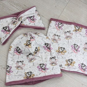 Puede incluir: Un conjunto de tres accesorios de invierno que incluye un gorro gris, un cuello de lana gris y una diadema gris. Los tres art&iacute;culos tienen un patr&oacute;n de hadas con alas rosas y amarillas sobre un fondo gris.