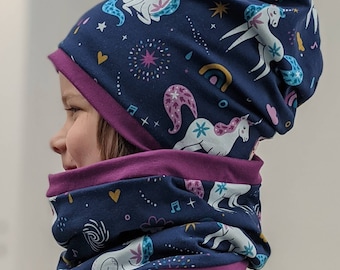 Puede incluir: Conjunto de gorro y braga de cuello azul marino con estampado de unicornios. La tela presenta unicornios blancos, arcoíris, estrellas y notas musicales. El conjunto tiene un ribete morado oscuro, creando un borde contrastante.