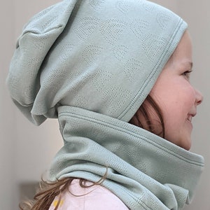 Puede incluir: Un gorro de punto verde claro con un cuello de punto a juego. El gorro tiene un patr&oacute;n texturizado y el cuello est&aacute; doblado.