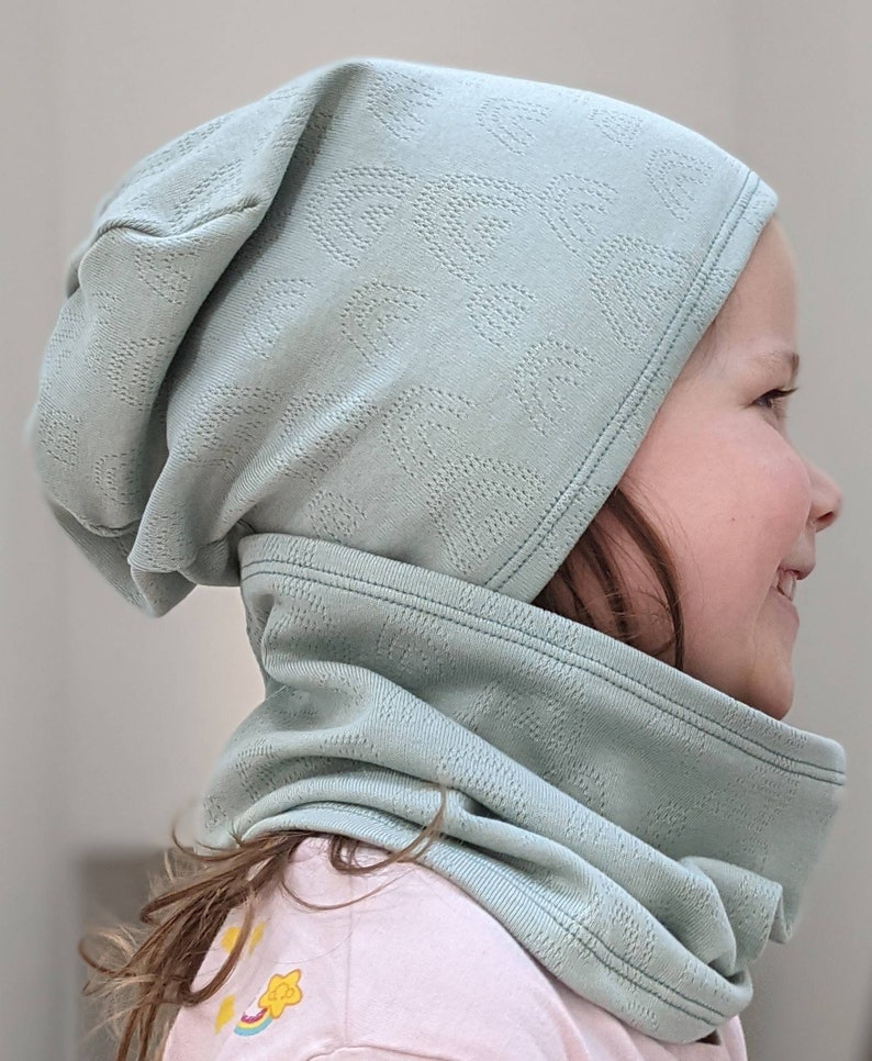 Puede incluir: Un gorro de punto verde claro con un cuello de punto a juego. El gorro tiene un patr&oacute;n texturizado y el cuello est&aacute; doblado.