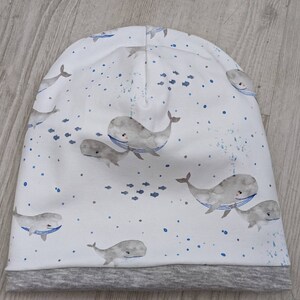 May include: White beanie with a gray brim featuring a repeating pattern of whales and fish. The whales are gray and white with blue outlines. The fish are blue.