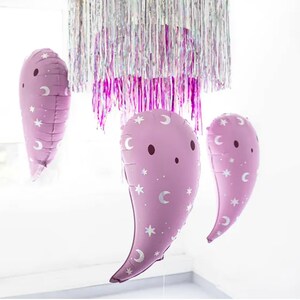 Puede incluir: Tres globos de color morado en forma de fantasma con estrellas blancas y medias lunas impresas en ellos. Los globos est&aacute;n colgados de un techo cubierto de oropel iridiscente.