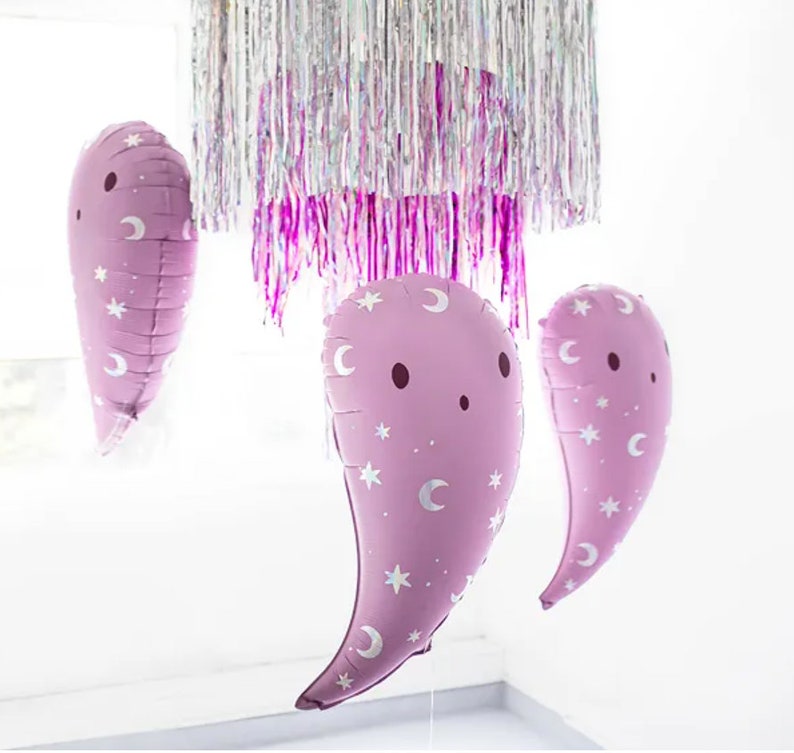 Puede incluir: Tres globos de color morado en forma de fantasma con estrellas blancas y medias lunas impresas en ellos. Los globos est&aacute;n colgados de un techo cubierto de oropel iridiscente.