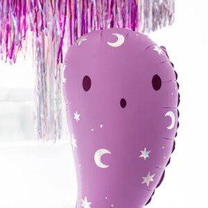 Puede incluir: Un globo morado en forma de fantasma con un patr&oacute;n de media luna y estrellas blancas. El globo tiene una cara simple con dos ojos negros y una peque&ntilde;a boca.