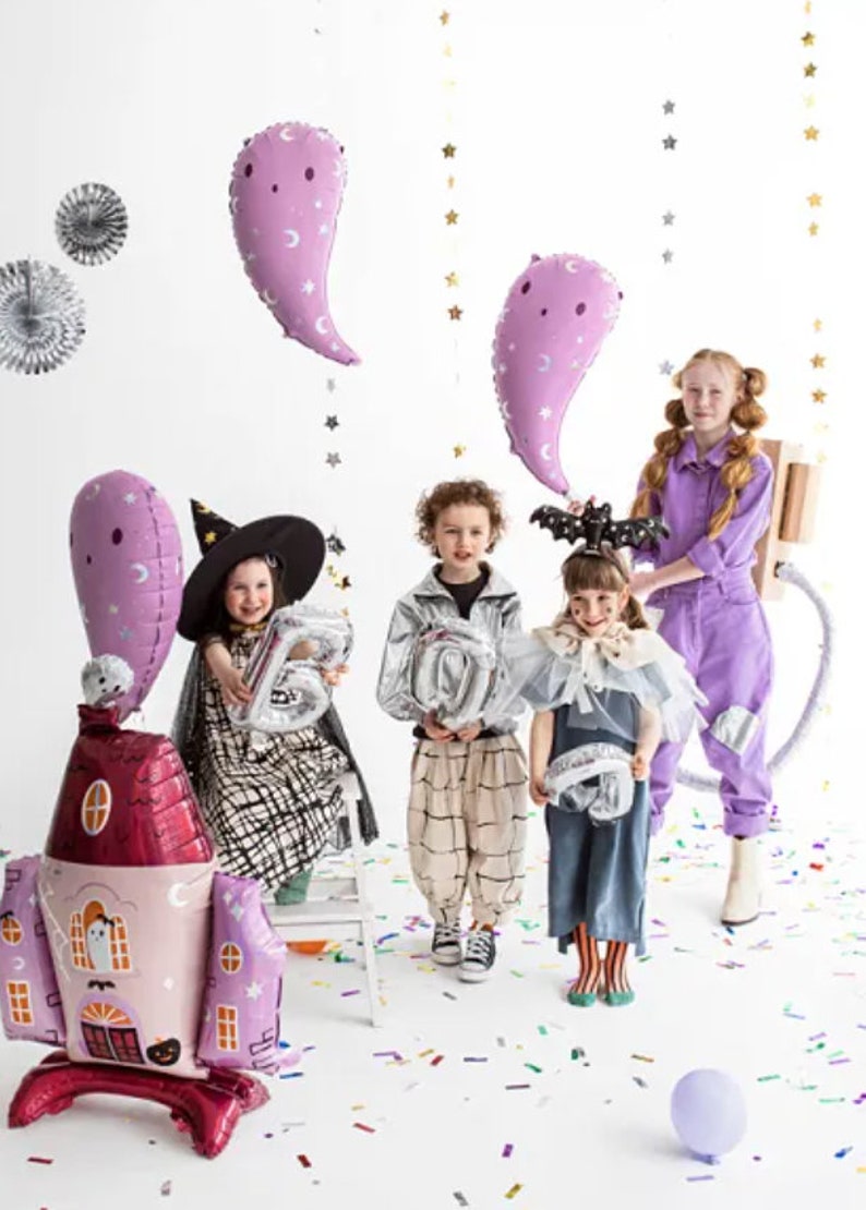 Puede incluir: Cuatro ni&ntilde;os disfrazados para Halloween sostienen varios globos. Los ni&ntilde;os llevan un disfraz de bruja, una chaqueta plateada, un vestido azul y un mono morado. Los globos tienen forma de fantasmas, n&uacute;meros y una casa. El fondo es blanco con confeti en el suelo.