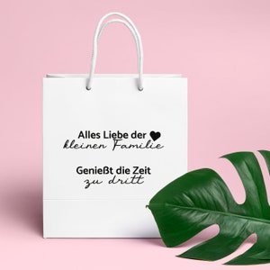 Puede incluir: Una bolsa de regalo blanca con un coraz&oacute;n negro y el texto "Alles Liebe der kleinen Familie Genie&szlig;t die Zeit zu dritt".