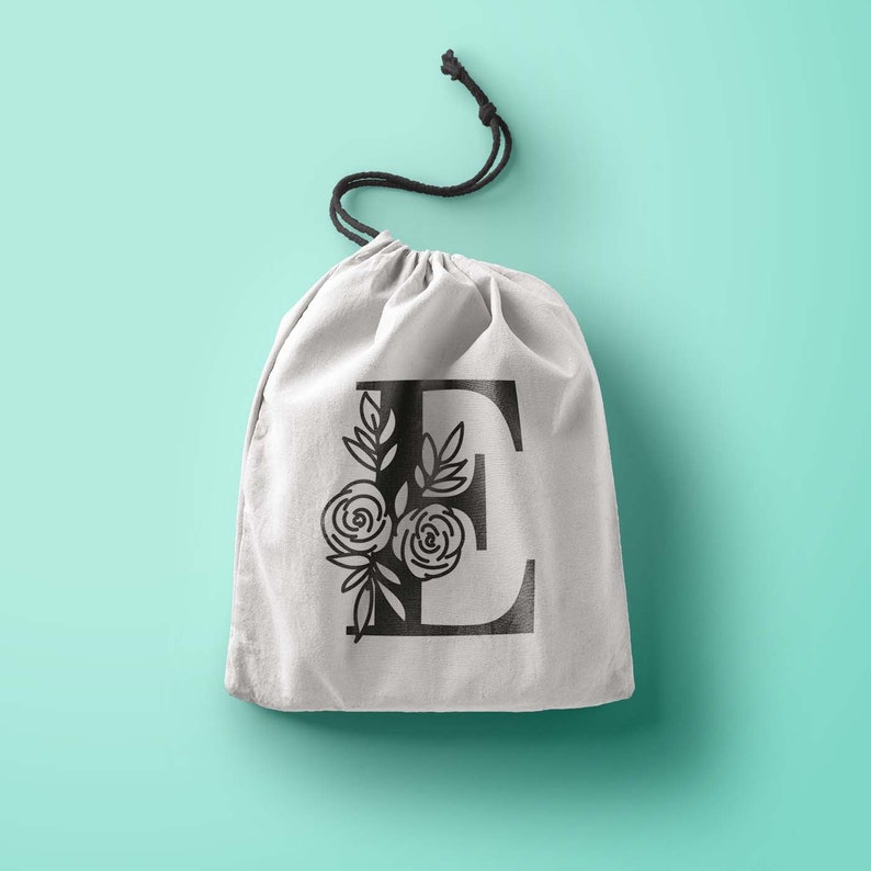 Może przedstawiać: Biała torba ze sznurkiem do ściągania z czarnym wzorem kwiatowym z literą "E" w środku.