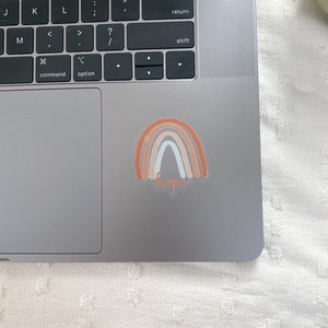 May include: A sticker with a rainbow design in shades of orange, pink, and blue with the word "hope" written in cursive underneath.
