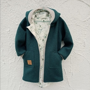 Può includere: Un cappotto con cappuccio color verde ottanio scuro con maniche lunghe e due tasche anteriori. L'interno è foderato con un tessuto chiaro con un motivo a foglie botaniche verdi. Una piccola etichetta quadrata marrone riporta made with love.