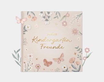 Può includere: Un libro quadrato con una copertina beige chiaro caratterizzata da un testo dorato in corsivo che recita "meine Kindergarten Freunde". La copertina è decorata con illustrazioni di fiori rosa e bianchi, foglie verdi e tre farfalle.