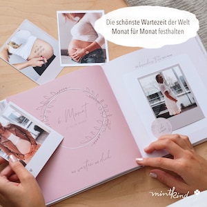 Pu&ograve; includere: Un diario di gravidanza rosa e bianco aperto su una pagina con il testo "6. Monat" e "Wir warten auf dich". Diverse foto di una persona incinta sono sparse intorno al diario. &Egrave; visibile anche il testo "Die sch&ouml;nste Wartezeit der Welt Monat f&uuml;r Monat festhalten".