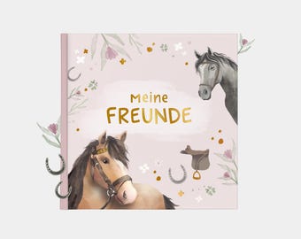 Può includere: Una copertina di libro quadrata con sfondo rosa chiaro presenta illustrazioni ad acquerello di cavalli, ferri di cavallo e elementi floreali. Il testo dorato recita "Meine FREUNDE". Il tema del libro è equestre.