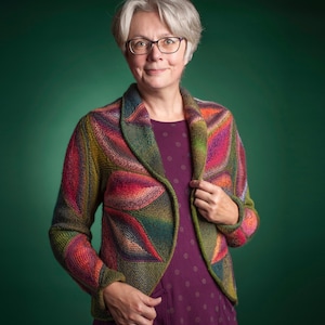 May include: A colorful, knitted jacket with a unique pattern. The jacket features a mix of red, green, orange, and purple hues. The woman in the image is wearing the jacket over a purple dress. The jacket has a shawl collar and a tailored fit.