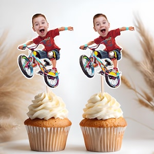 Peut inclure: Deux cupcakes avec un glaçage blanc surmontés d'un topper de cupcake personnalisé représentant un enfant sur un vélo coloré. Le visage de l'enfant est sur le topper.
