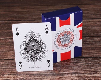 May include: A standard deck of playing cards with a black ace of spades card in the foreground. The card features an ornate design with a black spade in the center. The card box is blue with a red, white, and blue Union Jack design and the text "King Charles III Coronation 6th May 2023".