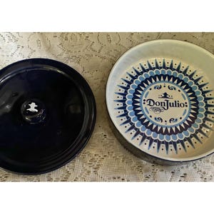 May include: A navy blue ceramic lid with a white emblem and a matching ceramic bowl. The bowl has a white interior with a blue and white geometric design and the text "Don Julio".