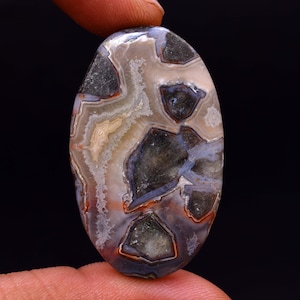 May include: A large, oval-shaped agate cabochon with a brown, white, and gray pattern. The agate has a unique, intricate design with a variety of colors and textures.