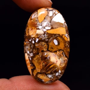 May include: Oval-shaped, translucent, brown, white, and yellow gemstone cabochon with a unique, intricate pattern of inclusions.