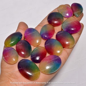 Può includere: Una collezione di gemme ovali e lucide, in una varietà di colori, dal rosso al viola, tenute in una mano. Le pietre, lunghe circa 2.5-5 cm, hanno una superficie liscia e brillante, mostrando sfumature arcobaleno.