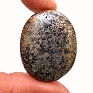 May include: A dark gray oval cabochon gemstone with a unique pattern of gold and green inclusions. The stone has a smooth, polished surface.