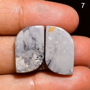 May include: A pair of white and grey agate cabochons with black and brown veins. The cabochons are shaped like a teardrop and have a smooth, polished surface.