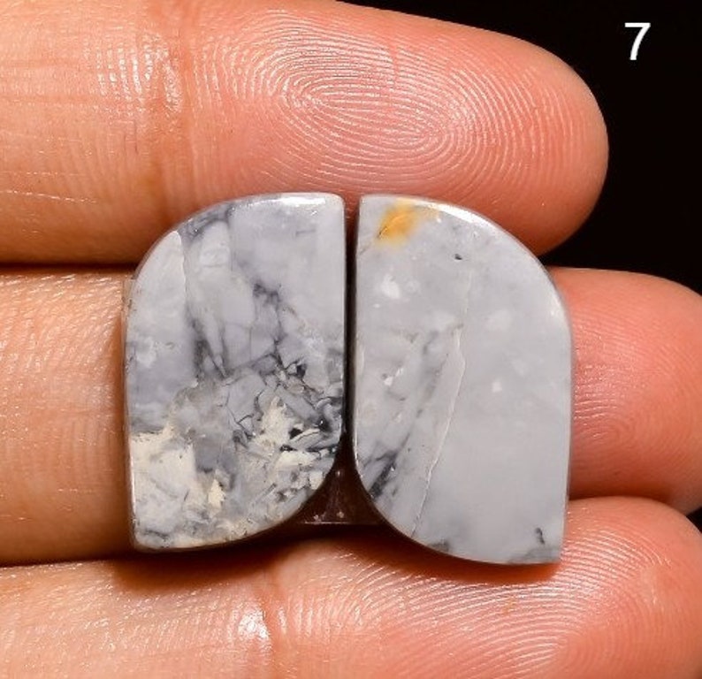 May include: A pair of white and grey agate cabochons with black and brown veins. The cabochons are shaped like a teardrop and have a smooth, polished surface.