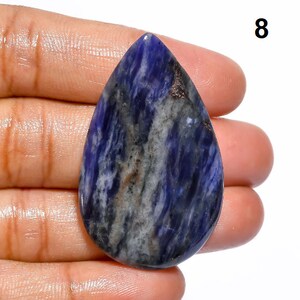 Op de afbeelding: Een traanvormige cabochon van blauwe, witte en grijze sodaliet met een glad, gepolijst oppervlak.