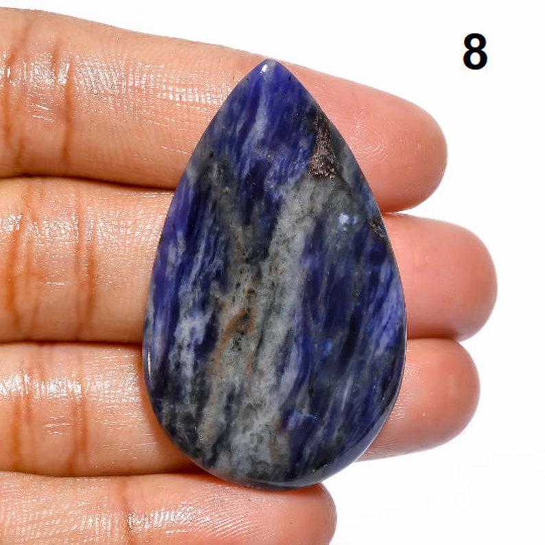Op de afbeelding: Een traanvormige cabochon van blauwe, witte en grijze sodaliet met een glad, gepolijst oppervlak.