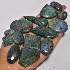 May include: A collection of 12 green, blue, and purple gemstone cabochons with red inclusions. The cabochons are various shapes and sizes, and are displayed on a hand.