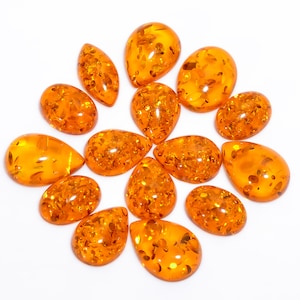 Peut inclure: Une collection de 14 pierres précieuses en forme de goutte d'ambre, chacune avec un motif unique d'inclusions. Les pierres sont disposées en cercle sur un fond blanc.