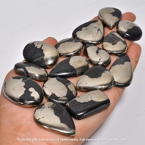 Pode incluir: Uma coleção de 13 cabochões de pirita em forma de pêra, pretos e prateados. As pedras têm uma superfície natural, áspera e texturizada.