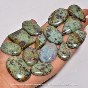 May include: A selection of polished gemstones in diverse shapes, such as ovals and teardrops. The stones display a mottled pattern of teal, brown, and red colours. The gemstones are presented on a light background.