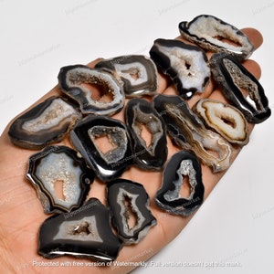 May include: A collection of black agate slices with natural crystal formations and a white interior. The slices have a smooth, polished surface and are arranged on a hand.