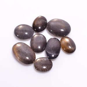 K&ouml;nnte beinhalten: Eine Sammlung von acht ovalen Sonnenstein-Cabochons in Braun- und Goldt&ouml;nen. Die Steine haben einen schimmernden, irisierenden Effekt.