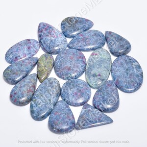 May include: A collection of 15 blue and red gemstone cabochons, some with a teardrop shape and others with a rounded oval shape. The stones have a speckled appearance with a mix of blue, red, and white.