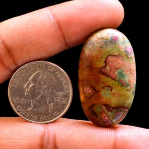 May include: A green, brown, and pink oval cabochon gemstone, approximately the size of a US quarter.