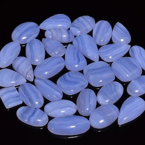 Pode incluir: Uma coleção de cabochões de ágata azul em várias formas e tamanhos. Os cabochões têm um acabamento liso e polido e exibem uma gama de tons azuis.