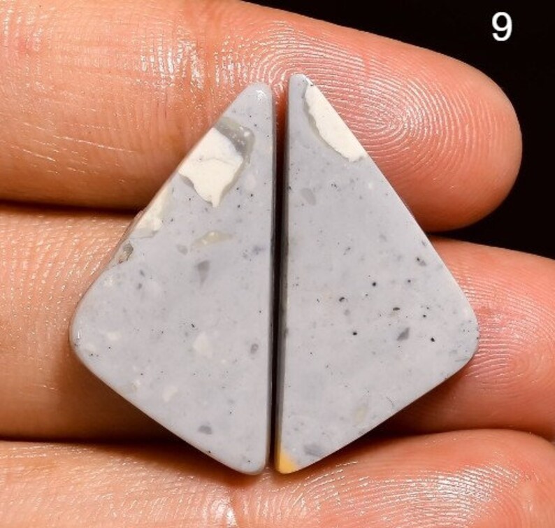 May include: Two triangular pieces of grey and white patterned stone, with a light yellow edge, are held in a hand. The stone has a speckled appearance.