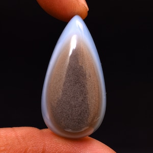 May include: A teardrop-shaped cabochon gemstone with a light blue outer layer and a brown and white inner layer.