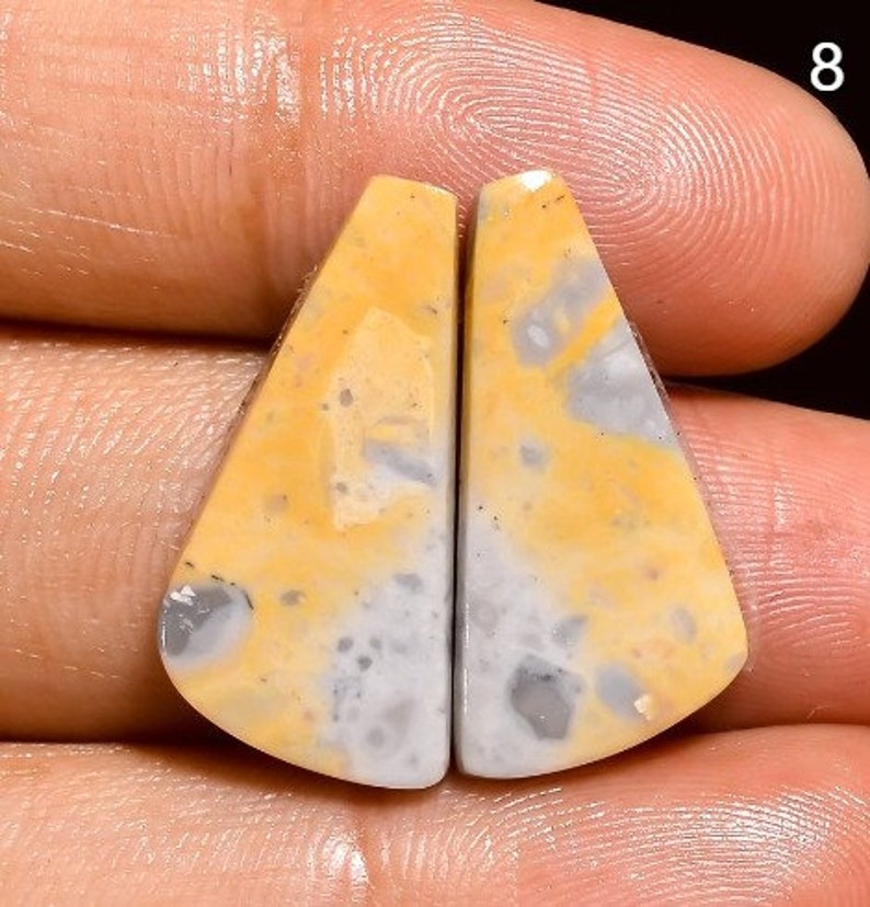 May include: A pair of yellow and white agate cabochons with a mottled pattern. The cabochons are shaped like triangles with rounded edges.