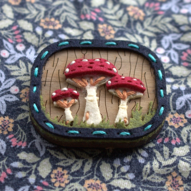 Mushroom brooch made from felt and wood shown fastened to someones top.